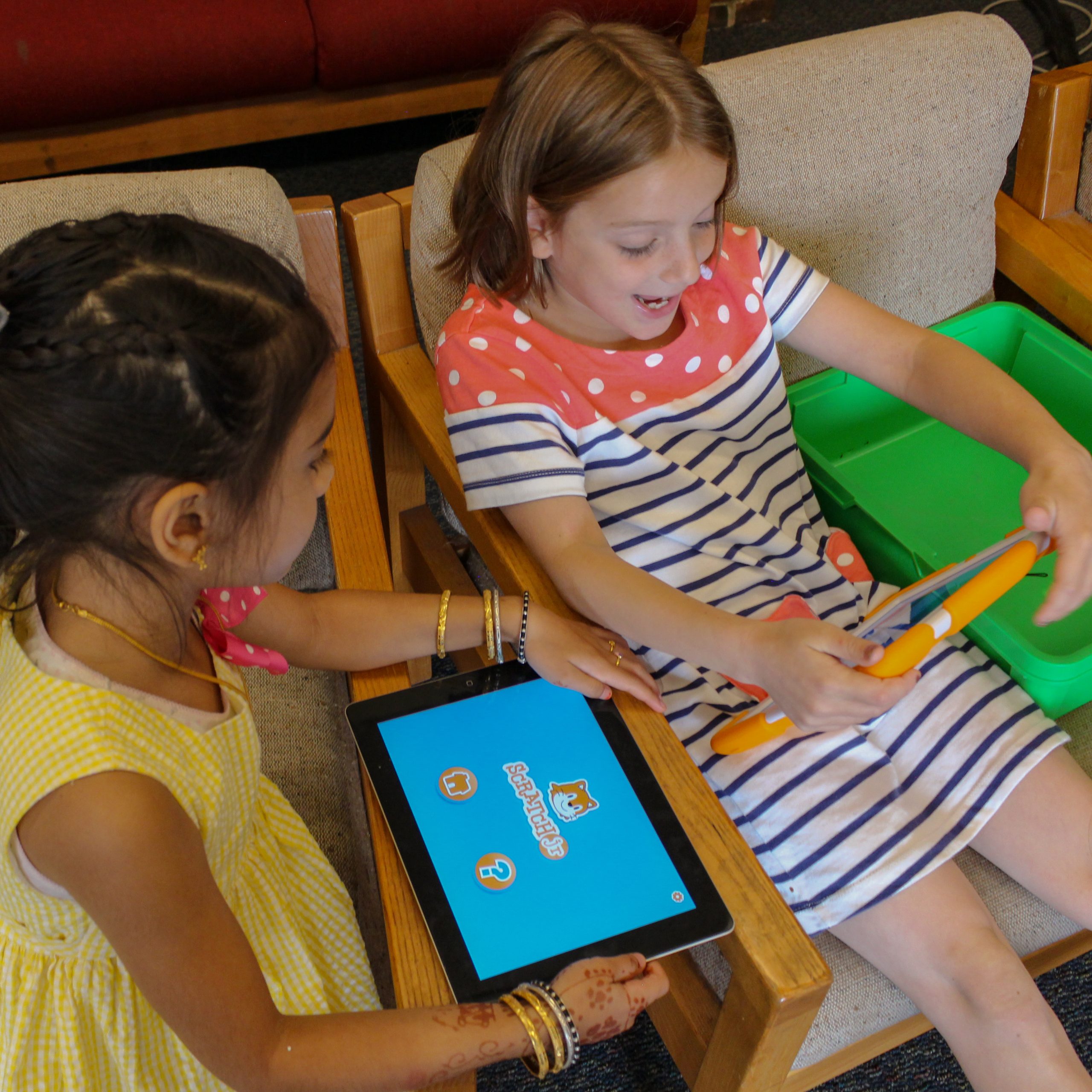 A photo of two young children each using iPads with the ScratchJr app open and smiling.
